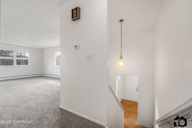 hallway with a textured ceiling, a baseboard heating unit, baseboards, and carpet floors