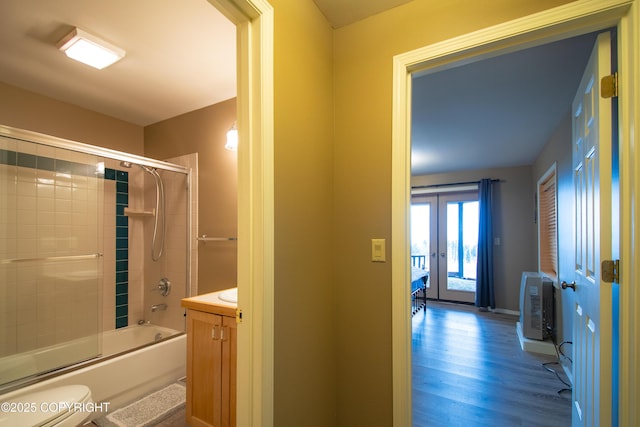 bathroom featuring toilet, french doors, wood finished floors, enclosed tub / shower combo, and vanity