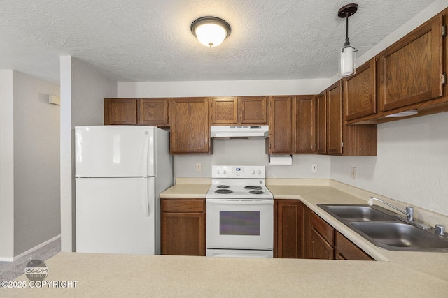 kitchen featuring under cabinet range hood, light countertops, hanging light fixtures, white appliances, and a sink