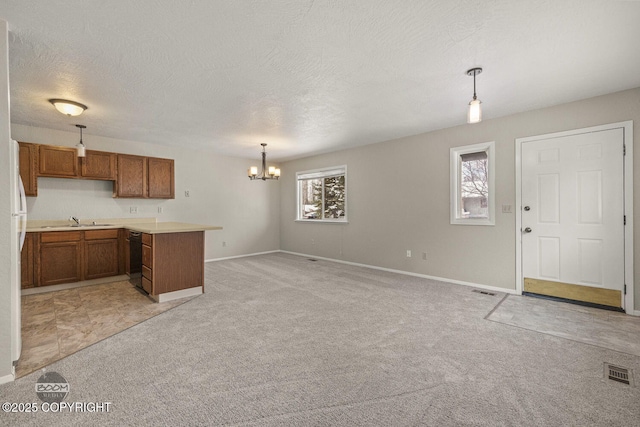 kitchen featuring light colored carpet, a peninsula, brown cabinetry, a notable chandelier, and a sink