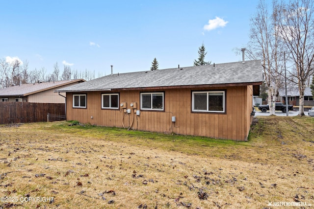 back of property featuring a yard, fence, and a shingled roof