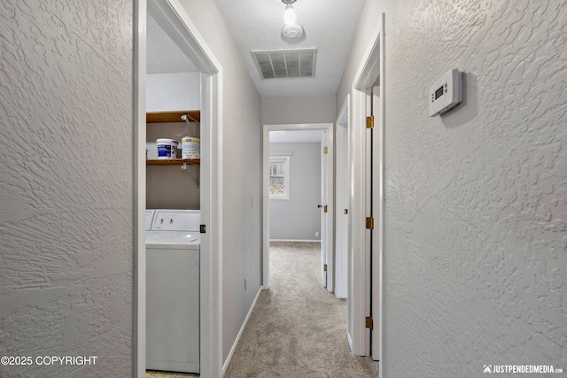 corridor featuring washer / clothes dryer, a textured wall, visible vents, and carpet floors