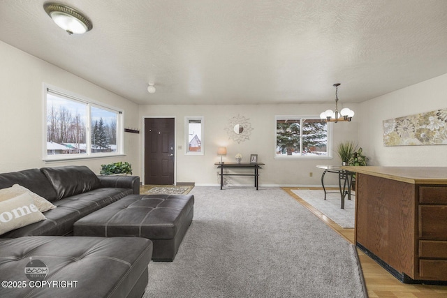 living area with a chandelier, light wood finished floors, a textured ceiling, and baseboards