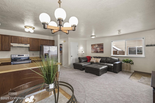 kitchen with a notable chandelier, under cabinet range hood, appliances with stainless steel finishes, light countertops, and light colored carpet