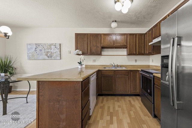 kitchen featuring light wood-type flooring, a sink, under cabinet range hood, appliances with stainless steel finishes, and a peninsula