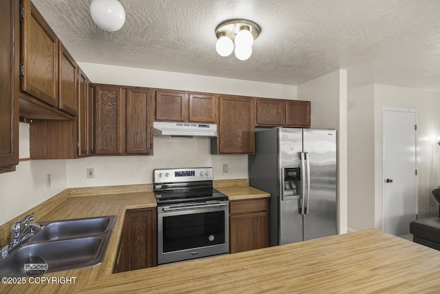 kitchen featuring a sink, a textured ceiling, under cabinet range hood, and stainless steel appliances