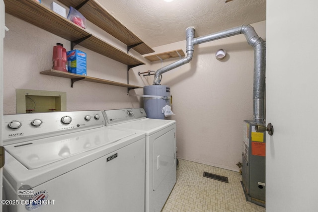 clothes washing area with a textured ceiling, laundry area, strapped water heater, and washer and clothes dryer