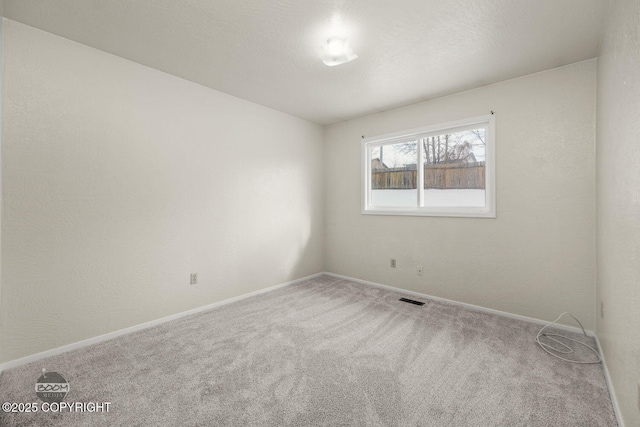 carpeted spare room featuring visible vents, baseboards, and a textured wall