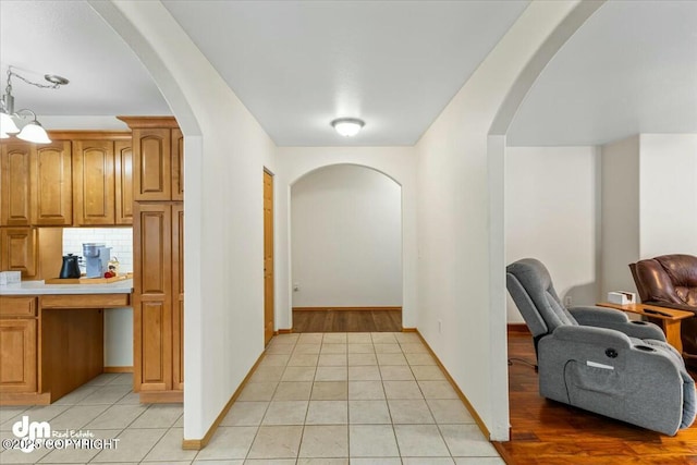 corridor with arched walkways, baseboards, and light tile patterned flooring