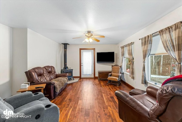 living room with baseboards, a wood stove, a ceiling fan, and wood-type flooring