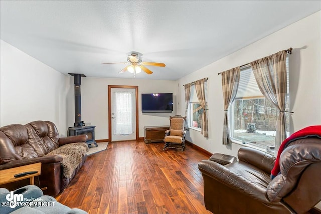 living area with hardwood / wood-style flooring, a wood stove, plenty of natural light, and a ceiling fan