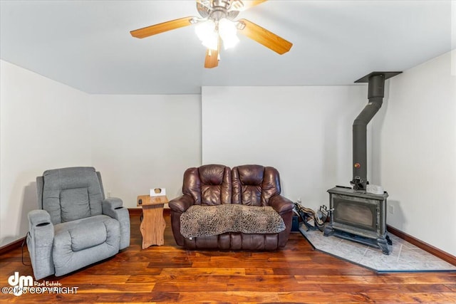 sitting room with a ceiling fan, a wood stove, wood finished floors, and baseboards