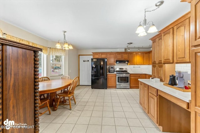 kitchen with backsplash, under cabinet range hood, stainless steel range with gas stovetop, black fridge, and an inviting chandelier