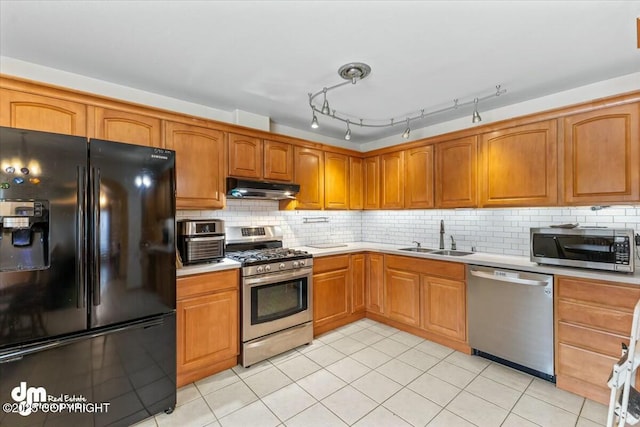 kitchen featuring under cabinet range hood, a sink, appliances with stainless steel finishes, light countertops, and decorative backsplash