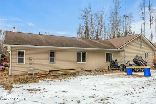 snow covered back of property with a shingled roof