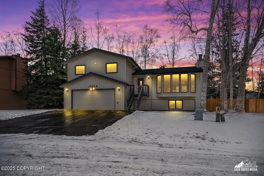split level home with an attached garage, fence, driveway, and a chimney