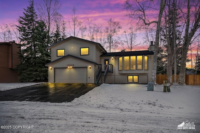 split level home with an attached garage, fence, driveway, and a chimney