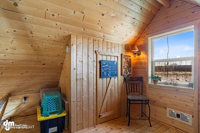 living area featuring visible vents, wooden walls, lofted ceiling, and hardwood / wood-style floors