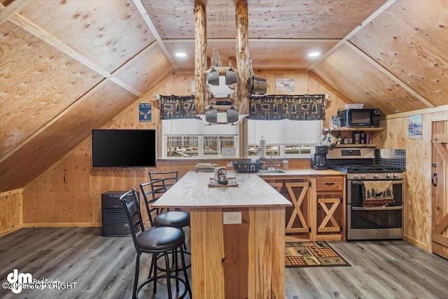 kitchen with double oven range, black microwave, wooden walls, wood finished floors, and lofted ceiling
