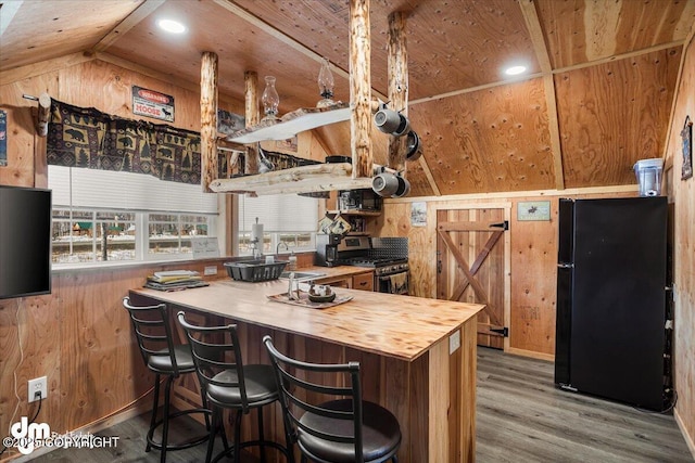 kitchen with wood walls, wood finished floors, stainless steel range with gas cooktop, a sink, and freestanding refrigerator