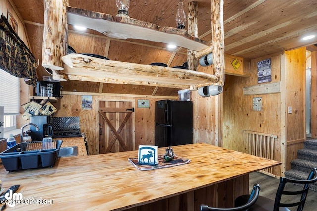 kitchen featuring wood walls, butcher block countertops, wood ceiling, a sink, and freestanding refrigerator