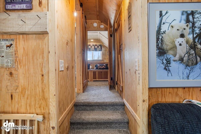 staircase with lofted ceiling, wooden walls, and carpet