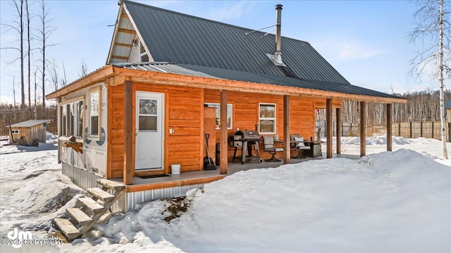 snow covered rear of property with metal roof and a porch