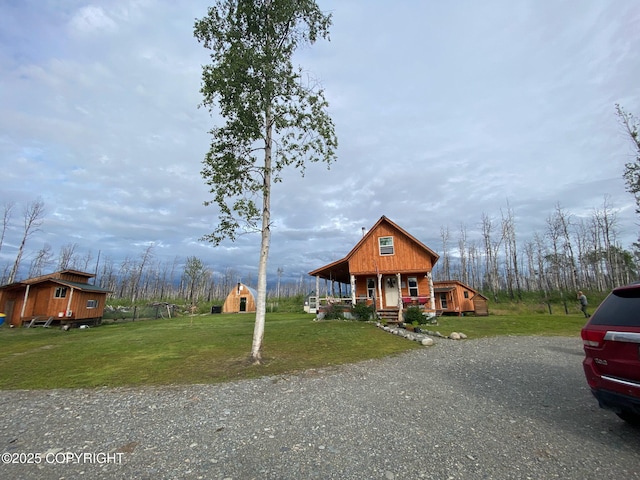chalet / cabin featuring a porch, an outdoor structure, a front yard, and driveway