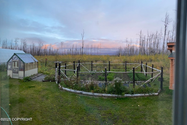 yard at dusk featuring an outbuilding, a greenhouse, fence, and a rural view