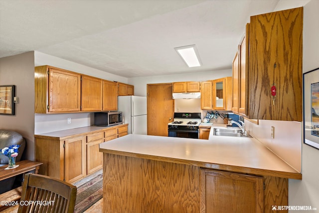 kitchen featuring freestanding refrigerator, a peninsula, gas range oven, stainless steel microwave, and a sink