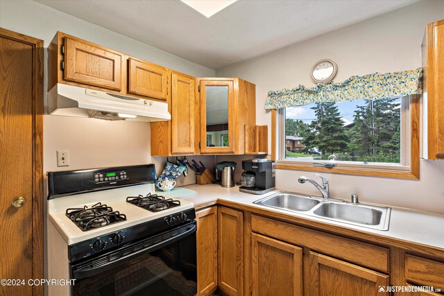 kitchen featuring brown cabinets, a sink, light countertops, range with gas stovetop, and under cabinet range hood