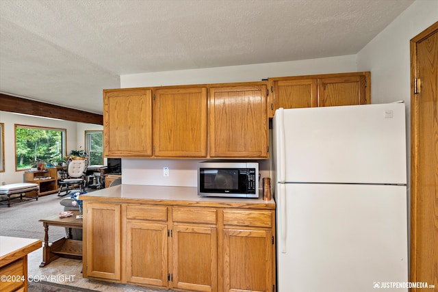 kitchen featuring light countertops, freestanding refrigerator, stainless steel microwave, and a textured ceiling