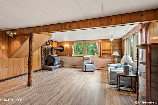 living room featuring a wood stove, wood finished floors, baseboard heating, and wood walls