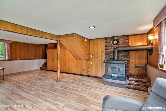 living area with wooden walls, a wood stove, baseboards, wood finished floors, and stairway