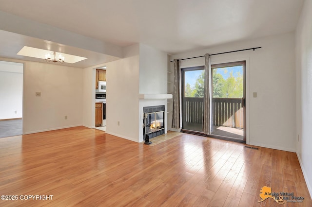 unfurnished living room featuring light wood-type flooring, a tiled fireplace, a chandelier, and baseboards