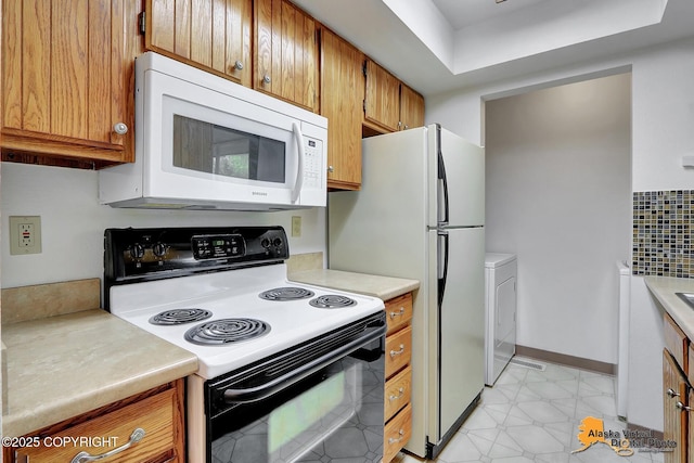 kitchen featuring white appliances, light countertops, brown cabinetry, washer / clothes dryer, and baseboards
