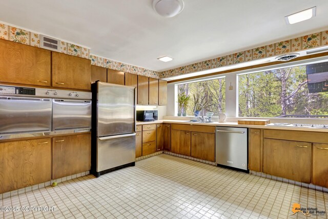 204 E 15th Ave, Anchorage, AK 99501 - kitchen featuring stainless steel appliances, brown cabinetry, light countertops, and wallpapered walls