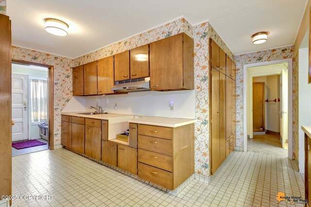 204 E 15th Ave, Anchorage, AK 99501 - kitchen featuring wallpapered walls, under cabinet range hood, brown cabinets, light countertops, and a sink