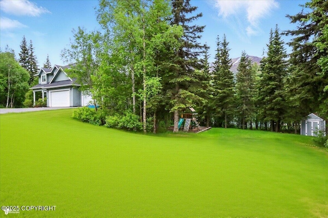 25656 Bendilent Cir, Eagle River, AK 99577 - view of green lawn featuring a playground, a garage, asphalt driveway, a mountain view, and a storage unit