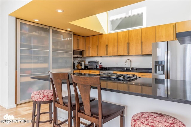 1382 Northbluff Dr # 4B, Anchorage, AK 99501 - kitchen featuring brown cabinets, stainless steel appliances, a sink, light wood-style floors, and a kitchen bar