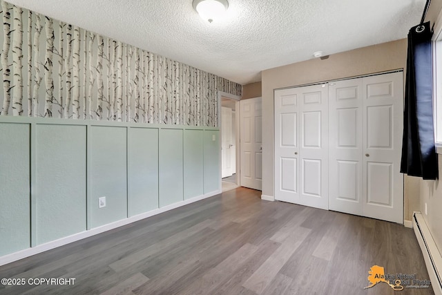 8400 E 11th Ct, Anchorage, AK 99504 - unfurnished bedroom with a baseboard heating unit, a textured ceiling, wood finished floors, a closet, and wallpapered walls