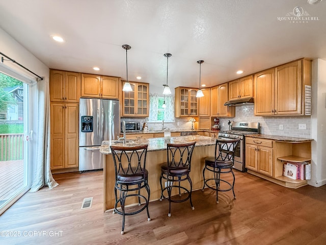 6934 Inlet Vista Dr, Wasilla, AK 99623 - kitchen with appliances with stainless steel finishes, under cabinet range hood, a center island, glass insert cabinets, and light stone counters