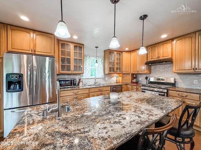 6934 Inlet Vista Dr, Wasilla, AK 99623 - kitchen featuring stainless steel appliances, a breakfast bar, under cabinet range hood, dark stone counters, and tasteful backsplash