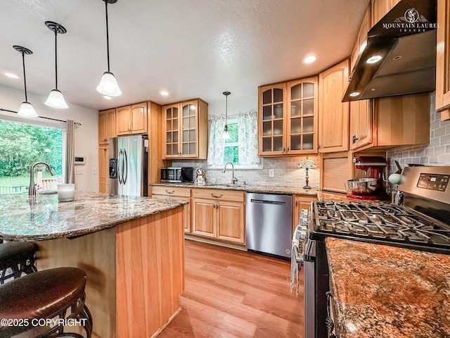 6934 Inlet Vista Dr, Wasilla, AK 99623 - kitchen with stainless steel appliances, range hood, a breakfast bar area, light stone countertops, and light wood-style floors
