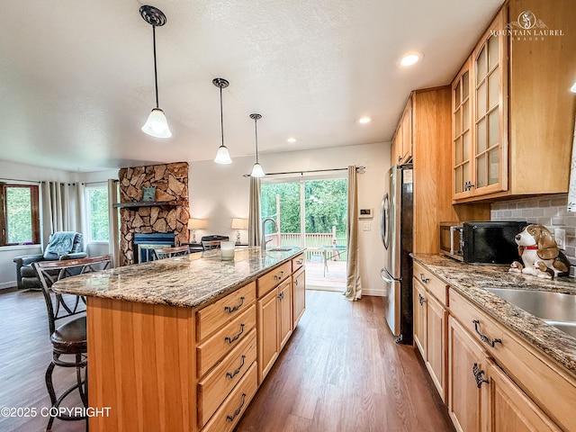 6934 Inlet Vista Dr, Wasilla, AK 99623 - kitchen featuring freestanding refrigerator, a breakfast bar, dark wood-style flooring, stone countertops, and a center island with sink