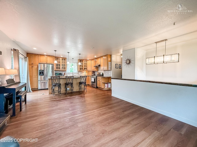 6934 Inlet Vista Dr, Wasilla, AK 99623 - kitchen featuring stainless steel appliances, wood finished floors, glass insert cabinets, a breakfast bar area, and a center island