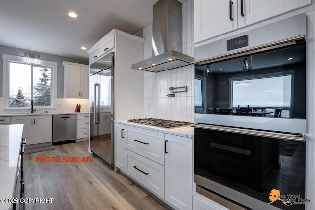 16074 Mountain Air Dr, Anchorage, AK 99516 - kitchen featuring stainless steel appliances, wall chimney range hood, a sink, tasteful backsplash, and white cabinets