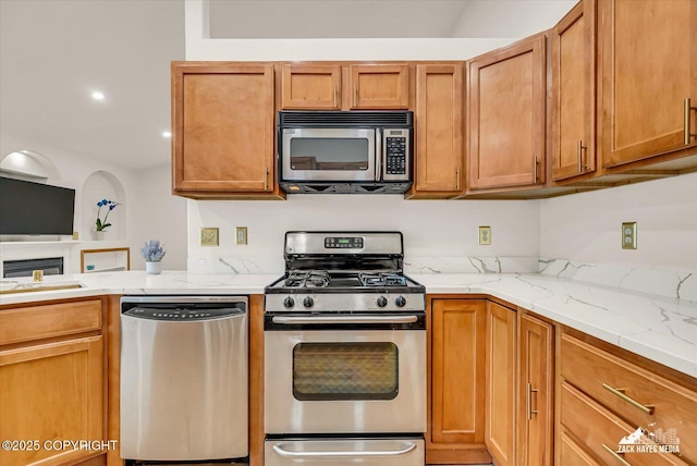11510 Tulin Park Loop, Anchorage, AK 99516 - kitchen featuring appliances with stainless steel finishes, light stone counters, brown cabinetry, and a fireplace