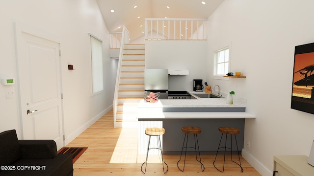 kitchen featuring a kitchen bar, a towering ceiling, a sink, and light wood-style floors