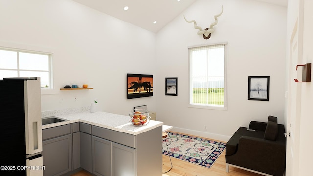 interior space with light wood finished floors, a peninsula, gray cabinetry, open shelves, and high vaulted ceiling